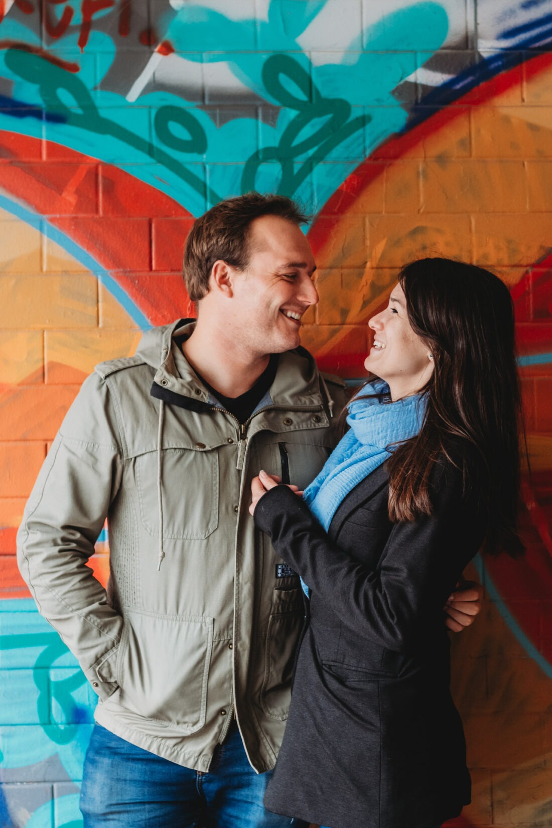 Young couple smiling at each other in front of colorful wall during a graffiti couple photo shoot in Prague.