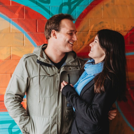 Young couple smiling at each other in front of colorful wall during a graffiti couple photo shoot in Prague.