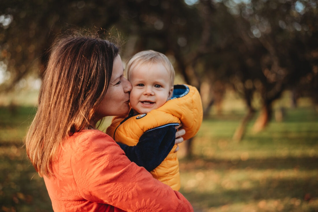 Mother kissing her toddler son during a tender autumn mom and me photo shoot.