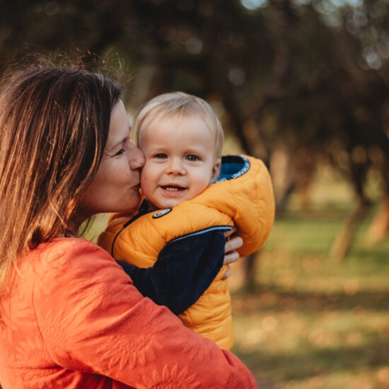 Mother kissing her toddler son during a tender autumn mom and me photo shoot.