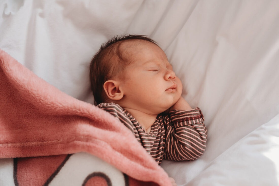 Newborn baby girl peacefully sleeping under a pink blanket.