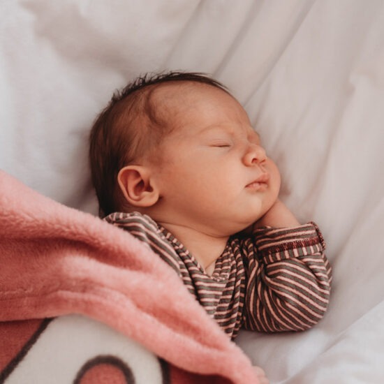 Newborn baby girl peacefully sleeping under a pink blanket.