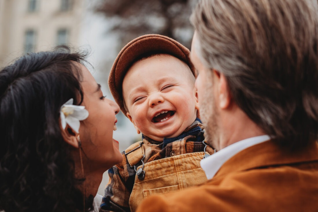 Laughing toddler held between smiling parents in Vienna city center during an expat family photo session.