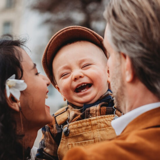 Laughing toddler held between smiling parents in Vienna city center during an expat family photo session.