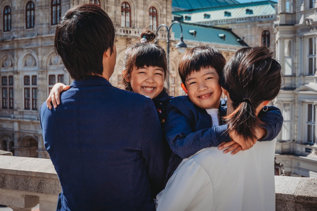 Smiling kids held by parents with State Opera in the background - farewell photo shoot in Vienna at its finest.