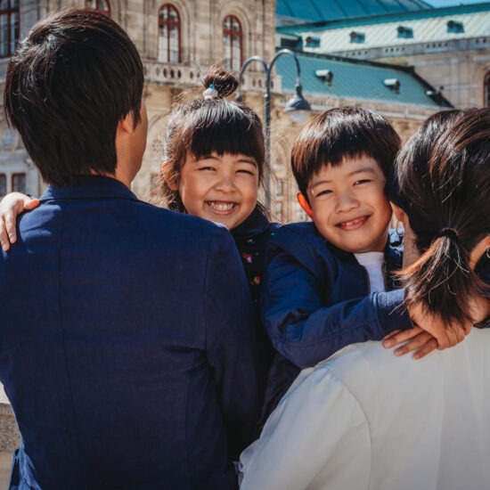 Smiling kids held by parents with State Opera in the background - farewell photo shoot in Vienna at its finest.