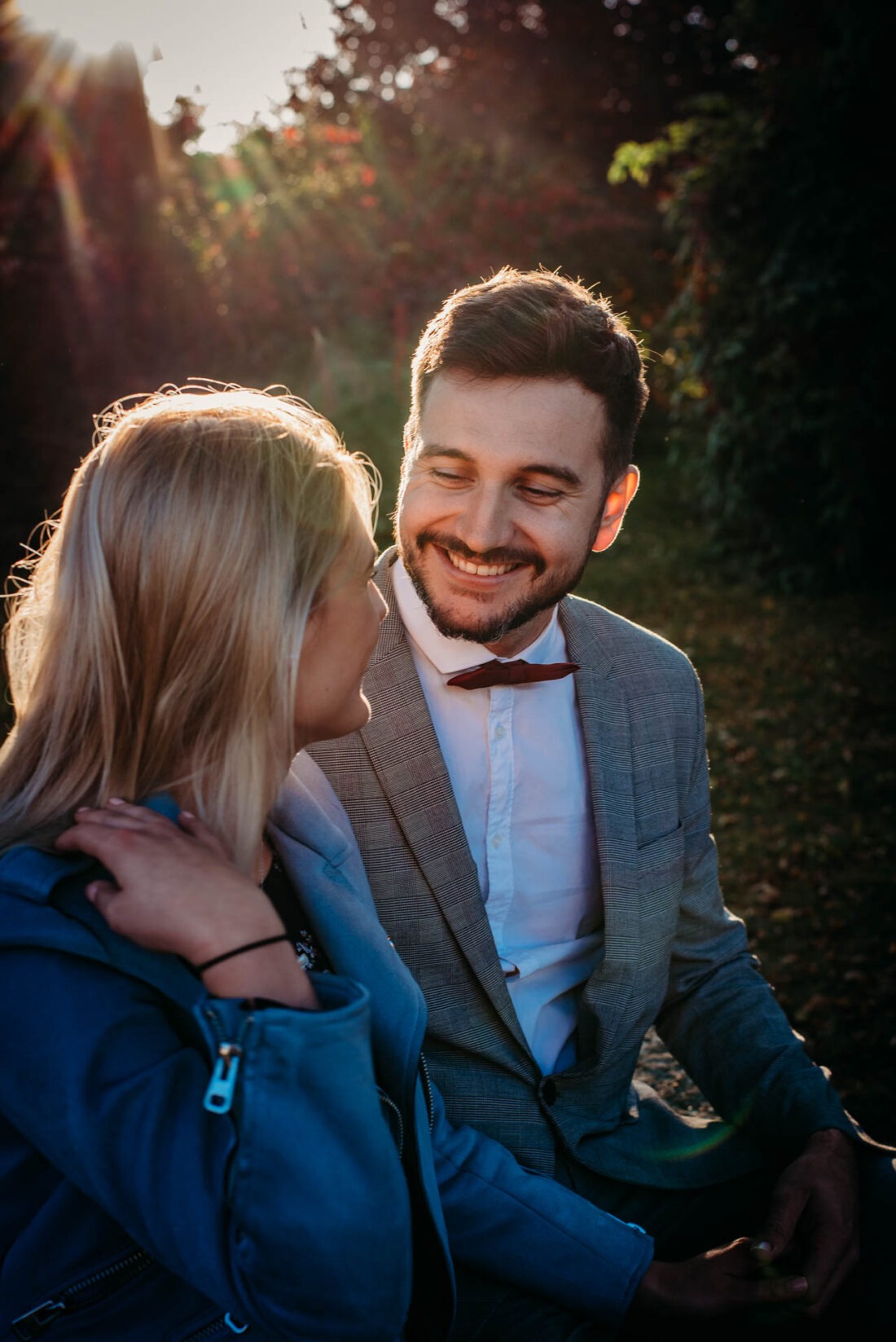 Couple sharing a smile while standing close under fall trees.