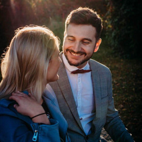 Couple sharing a smile while standing close under fall trees.