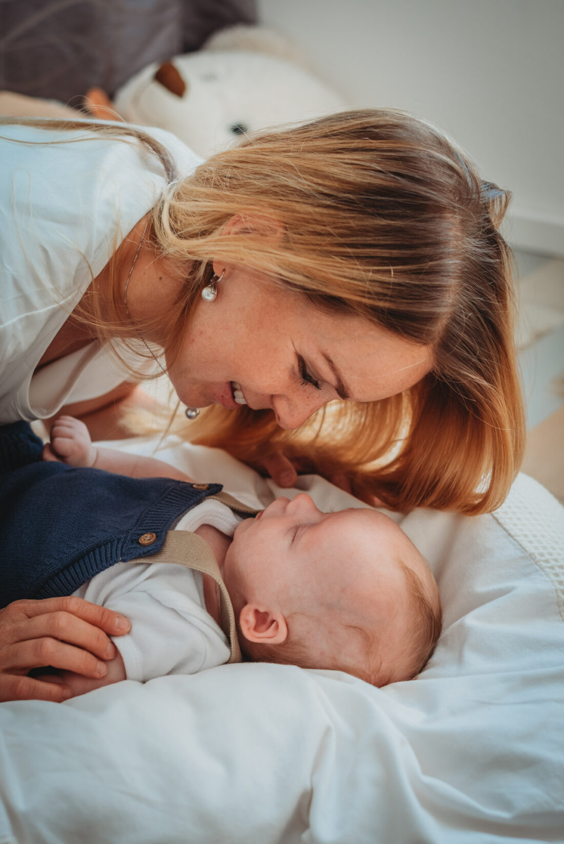 Mom smiling at her newborn baby boy while lying face to face on a bed.