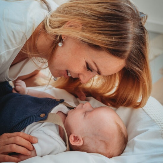 Mom smiling at her newborn baby boy while lying face to face on a bed.