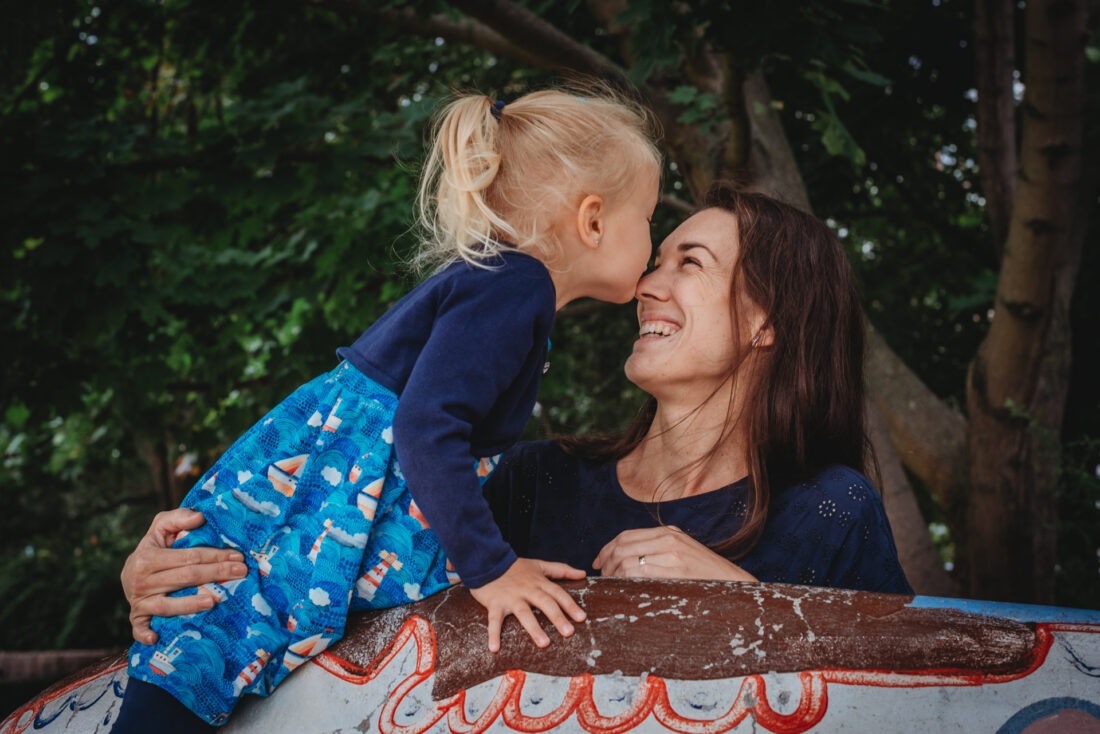 Blonde toddler kissing her mom’s nose during outdoor photo shoot in Pilsen, Czech Republic.