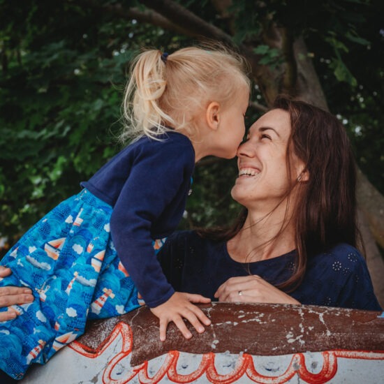 Blonde toddler kissing her mom’s nose during outdoor photo shoot in Pilsen, Czech Republic.
