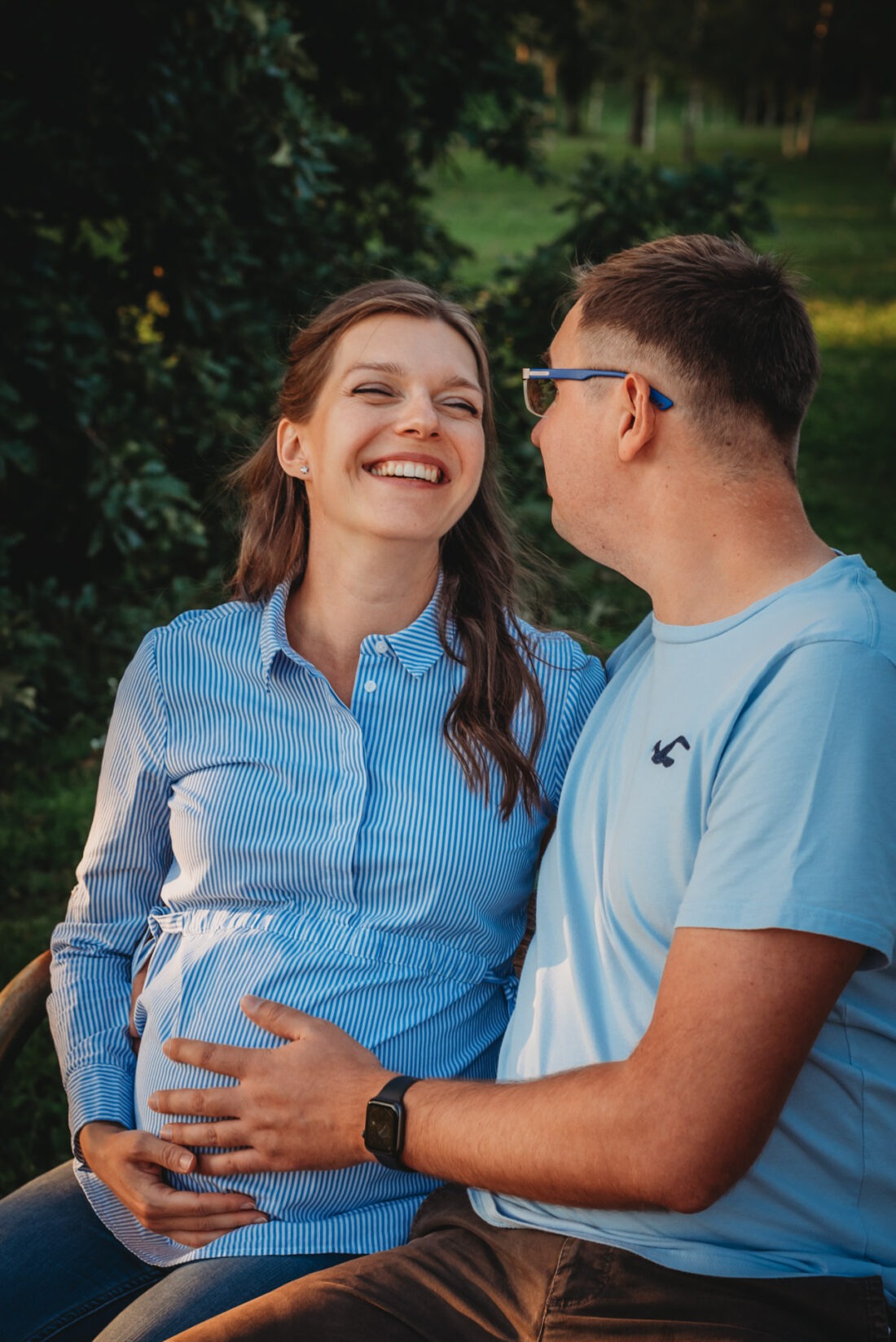 Shy expecting couple smiling during a sunset pregnancy photo shoot in Kurpark Oberlaa in Vienna.