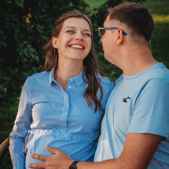 Shy expecting couple smiling during a sunset pregnancy photo shoot in Kurpark Oberlaa in Vienna.
