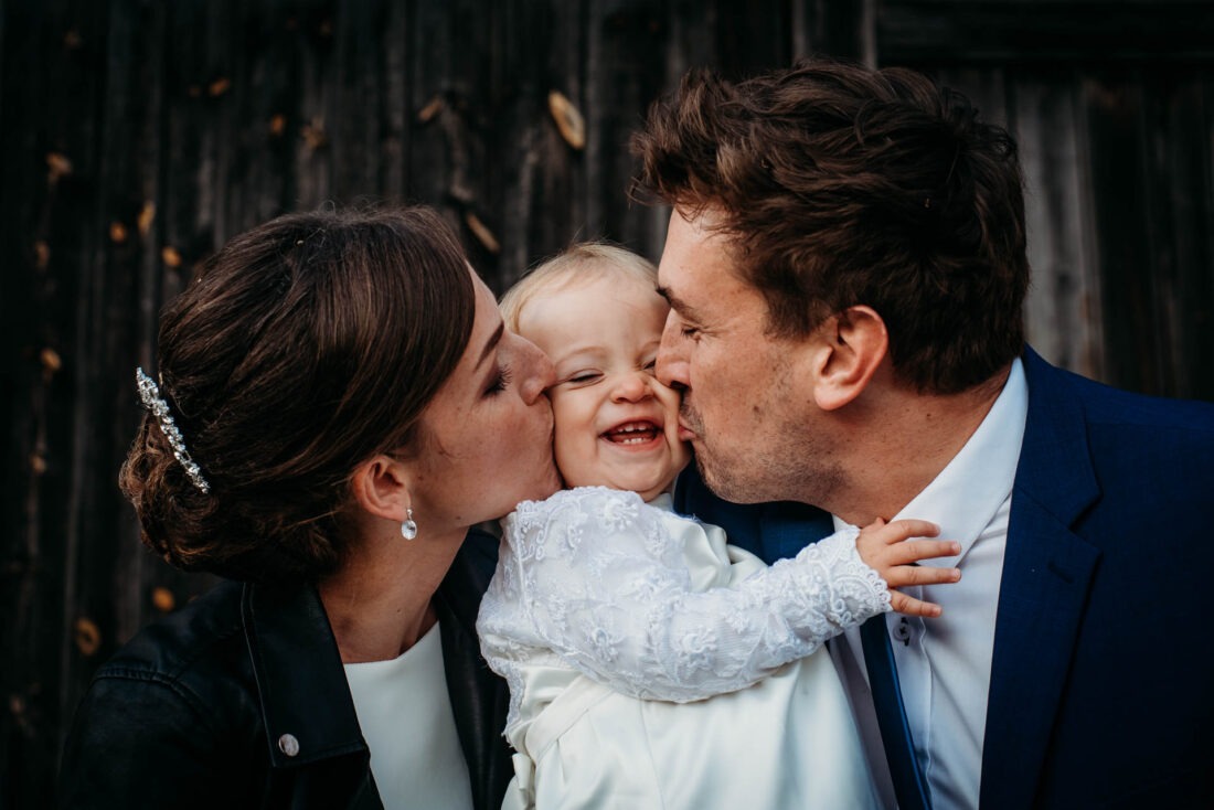Bride and groom kissing their baby daughter on the cheeks during wedding.