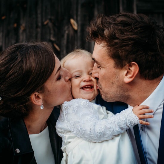 Bride and groom kissing their baby daughter on the cheeks during wedding.