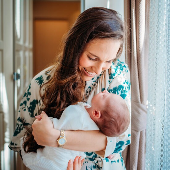 Smiling mother cradling her newborn by a sunlit window.