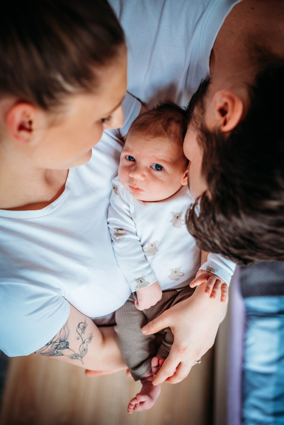 A newborn baby lying in the arms of both parents as they look down at him, capturing a close and intimate moment.