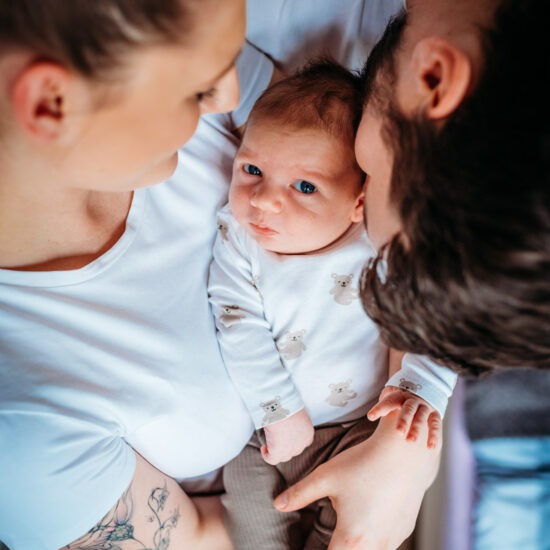 A newborn baby lying in the arms of both parents as they look down at him, capturing a close and intimate moment.