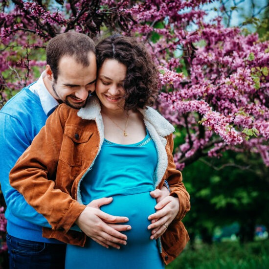 Couple cuddling under blooming pink spring blossoms in Donau Park.