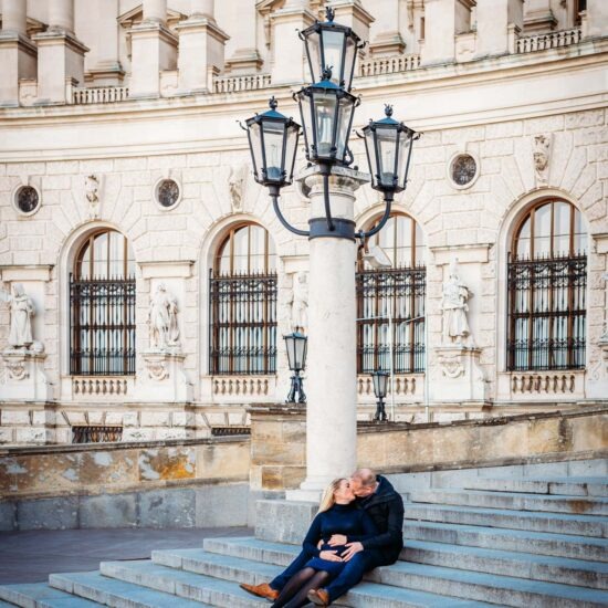 A pregnant couple sitting on the grand stairs of Hofburg Palace, enjoying their time together during their pregnancy photoshoot in Vienna.