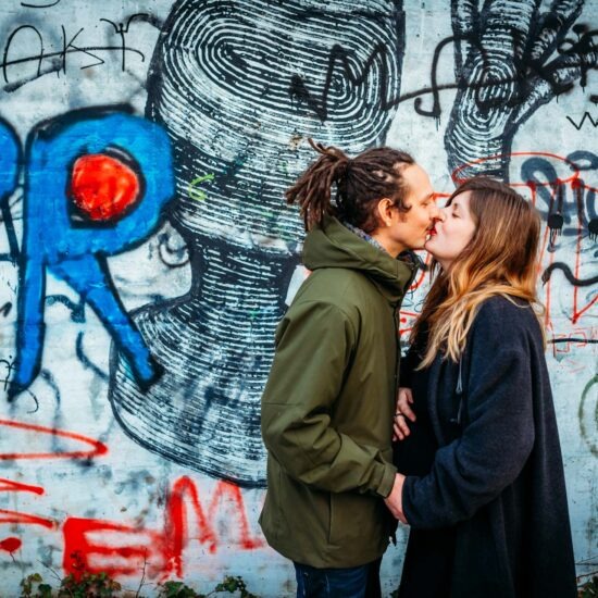 An expecting couple shares a kiss in front of a graffiti wall, blending maternity photography with an urban feel.