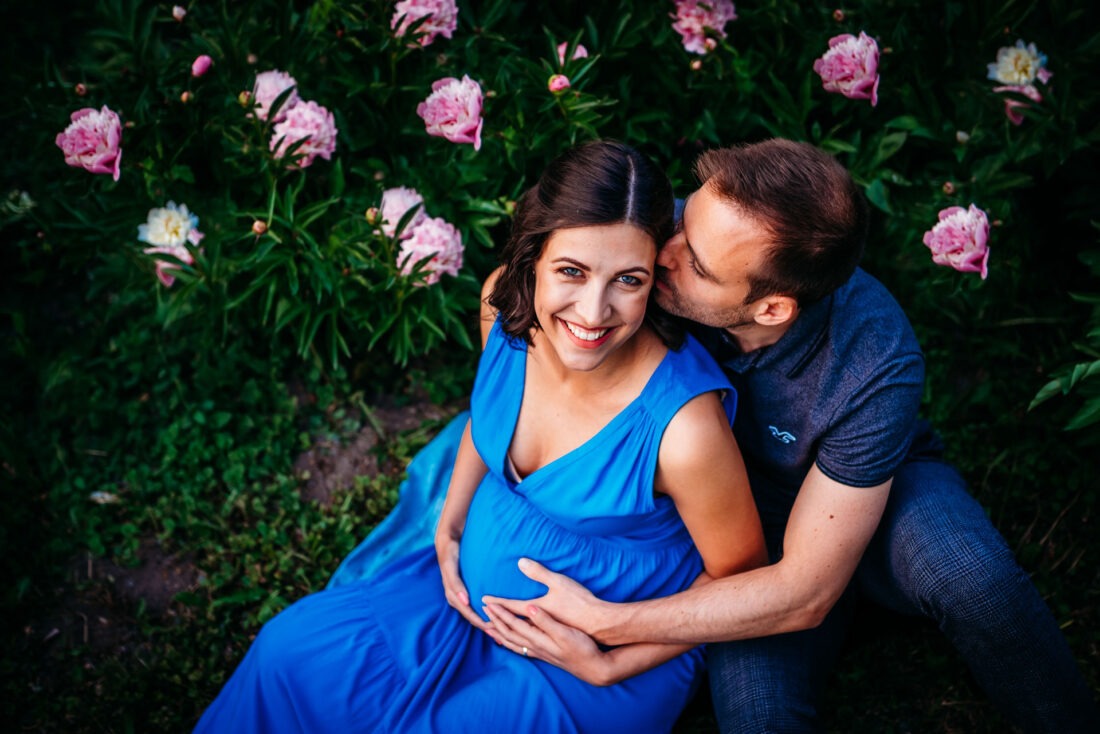 Smiling pregnant woman with partner sitting in flower garden of Donau Park.