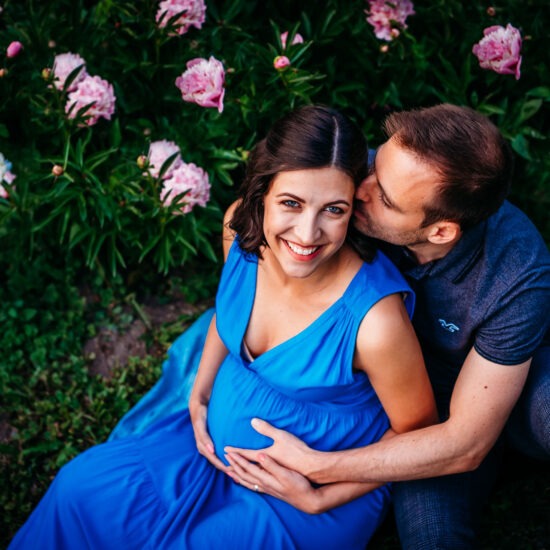 Smiling pregnant woman with partner sitting in flower garden of Donau Park.
