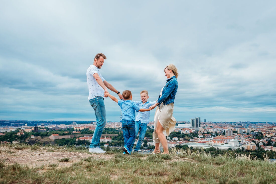 A happy family of four spinning in a circle during an outdoor family photoshoot in Prague.