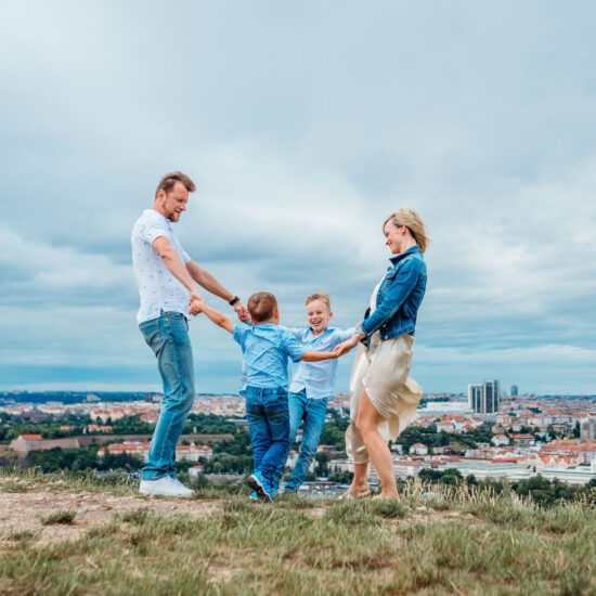 A happy family of four spinning in a circle during an outdoor family photoshoot in Prague.