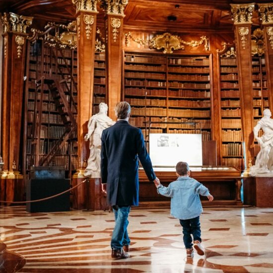 Father and son walking hand in hand in the Prunksaal, Austrian National Library, exploring the history of Vienna.