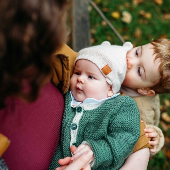 A sweet moment as a toddler kisses his newborn sister during an outdoor family photoshoot in Vienna.
