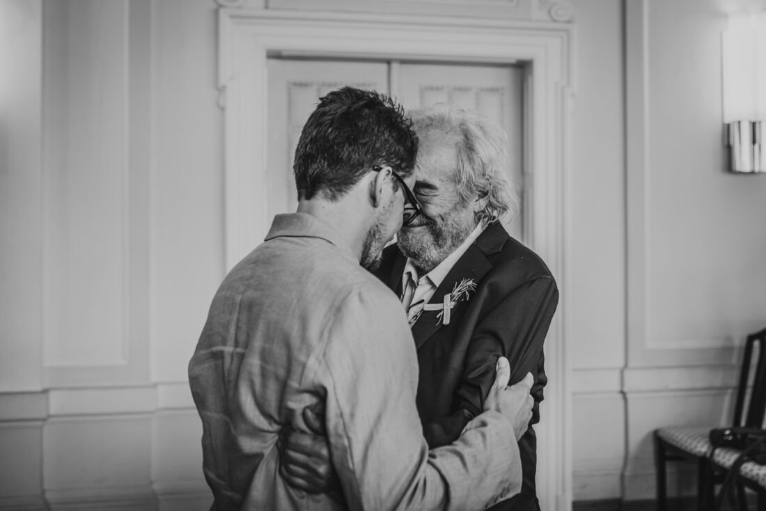 Black and white photo of the groom’s grandfather congratulating his grandson at his civil wedding in Vienna, holding back tears in an emotional moment."