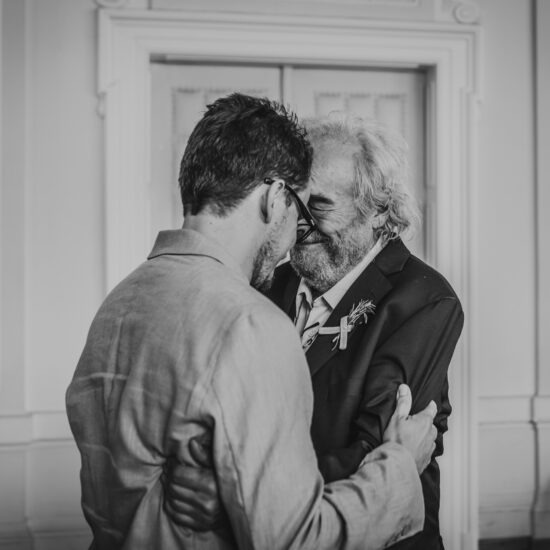Black and white photo of the groom’s grandfather congratulating his grandson at his civil wedding in Vienna, holding back tears in an emotional moment."