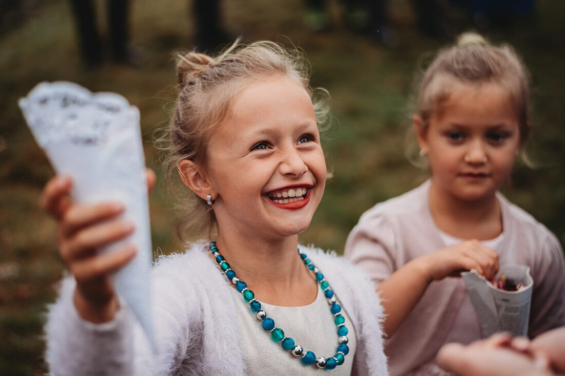 Young flower girl excitedly holding a cone of petals, ready to toss them in celebration.