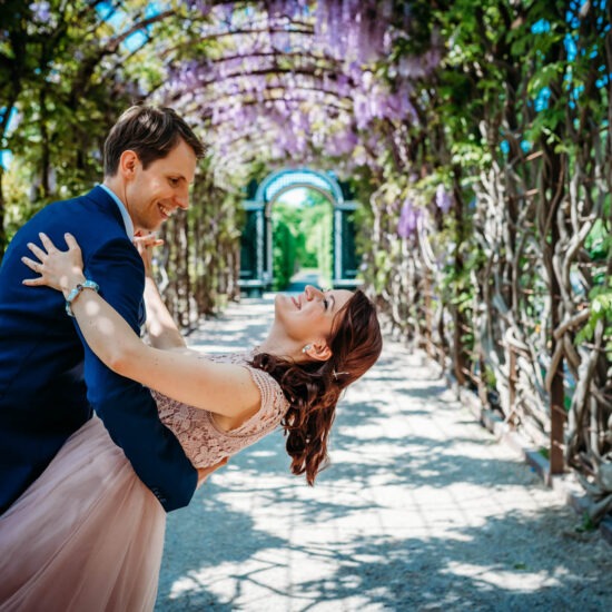Groom playfully dips the bride while she laughs, under a beautiful floral archway.