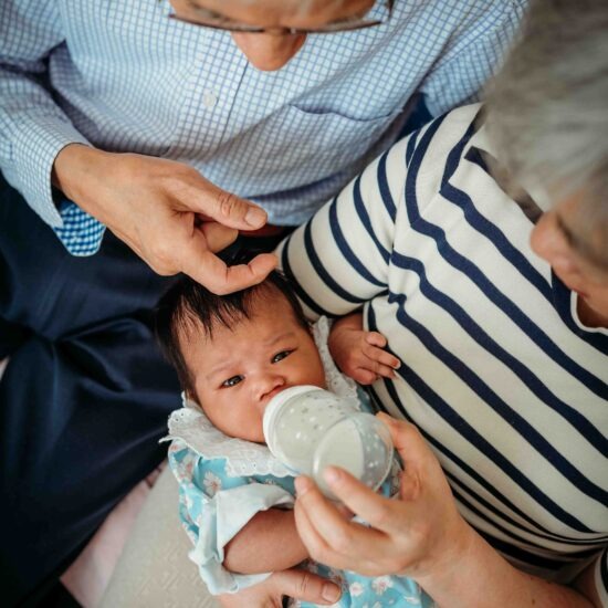 A bird’s-eye view of a newborn drinking milk while being cradled by their grandparents.