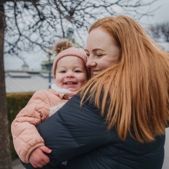 A mother in a black winter coat holds her smiling toddler daughter, dressed in a pink winter outfit, in Vienna’s city center.