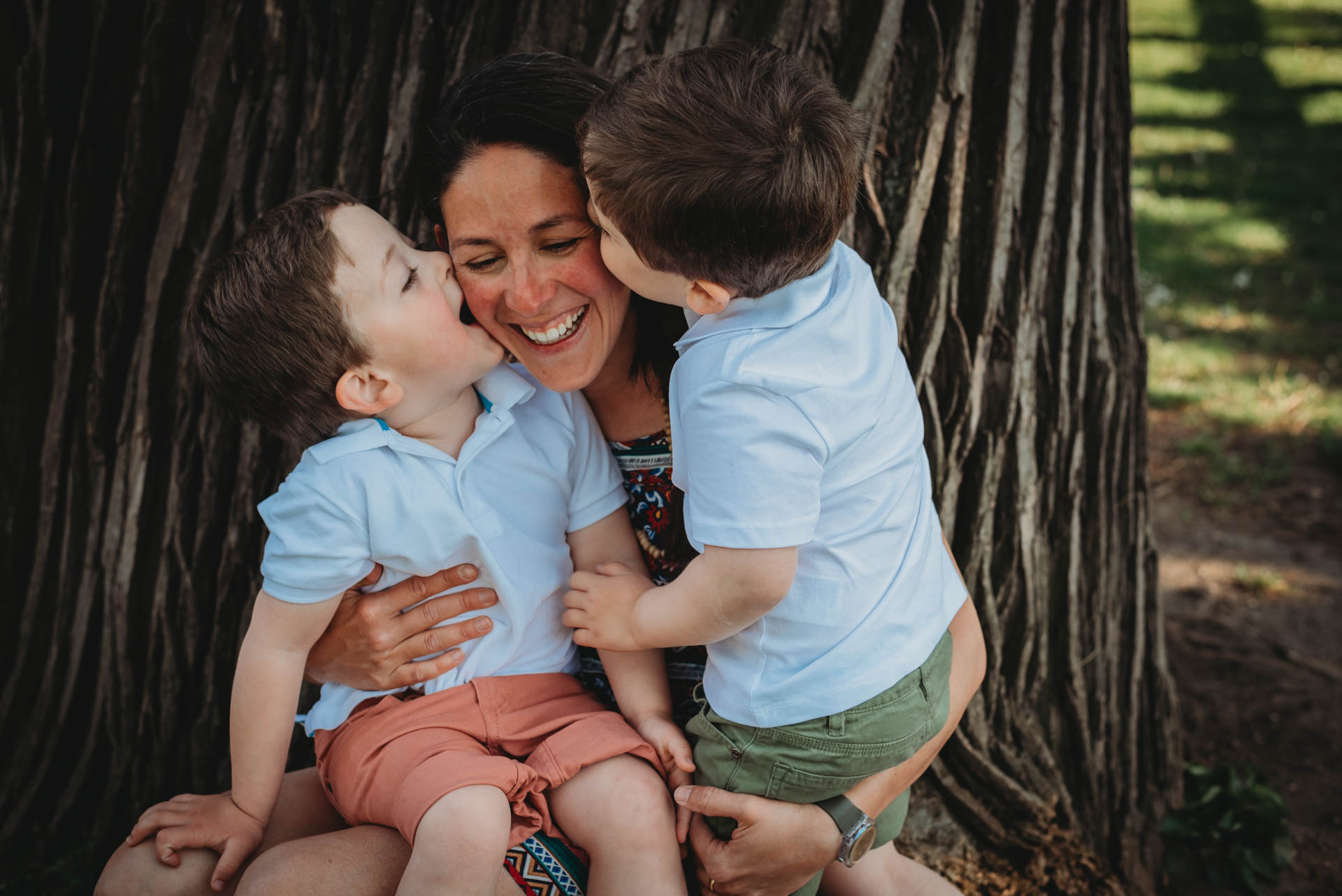 Mom smiling while receiving kisses from her twin boys during spring photo shoot in Stadtpark, Vienna.
