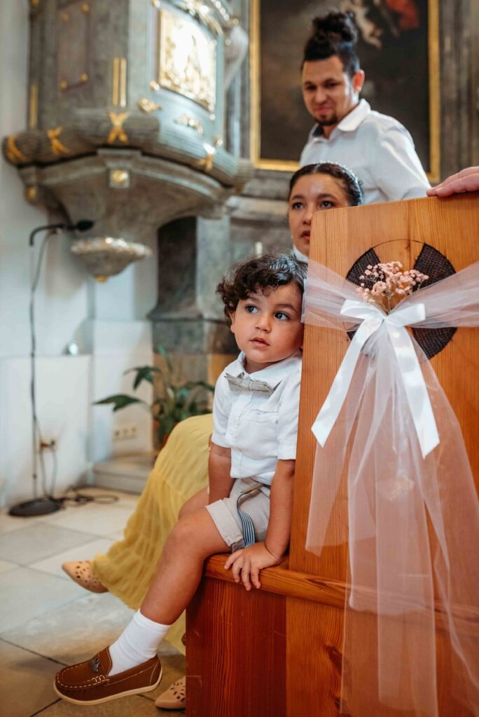 little-brazilian-boy-sitting-church-aisle-vienna Little boy sitting in church pew during baptism ceremony in Vienna