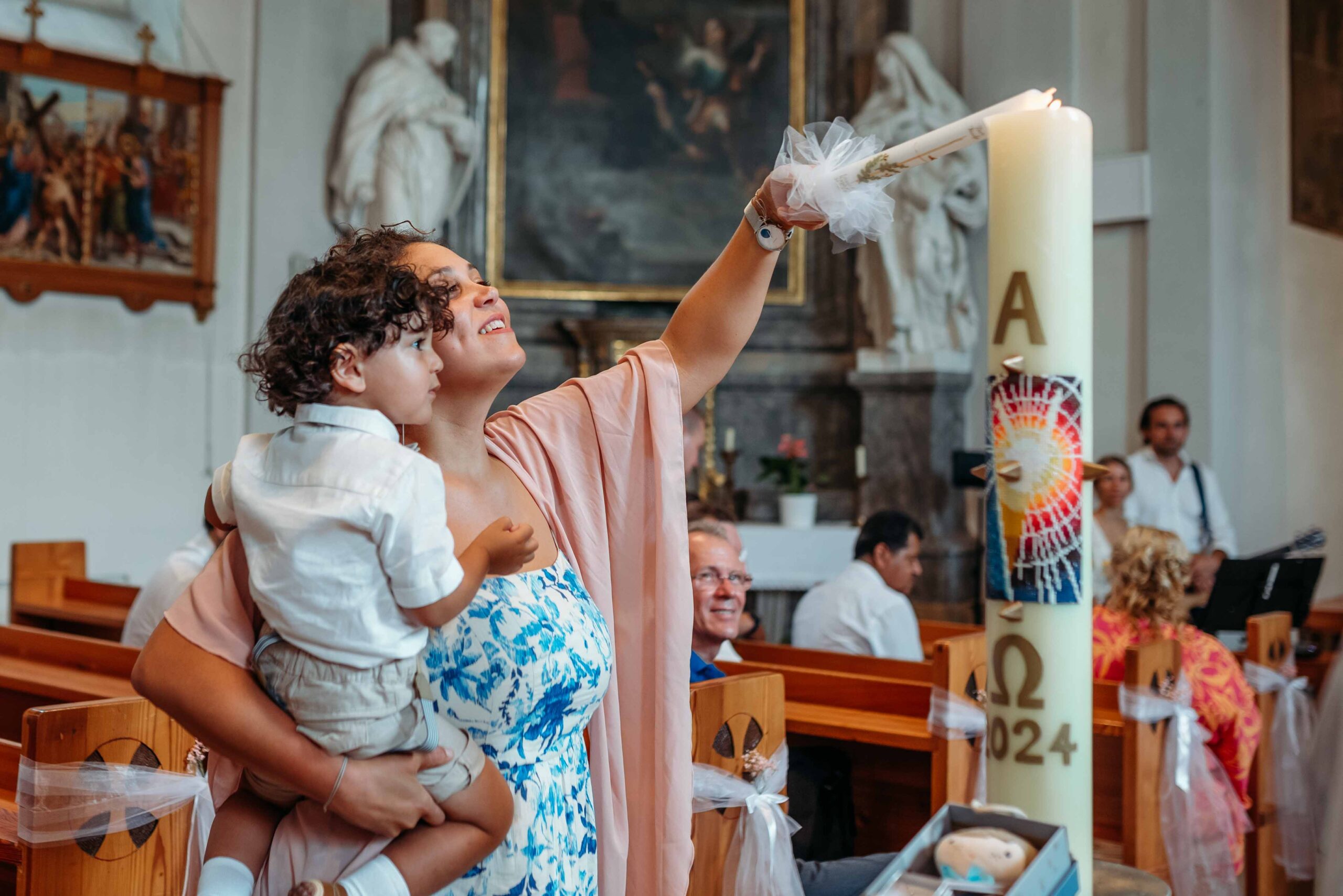 Godmother holding child while lighting baptism candle in church in Vienna