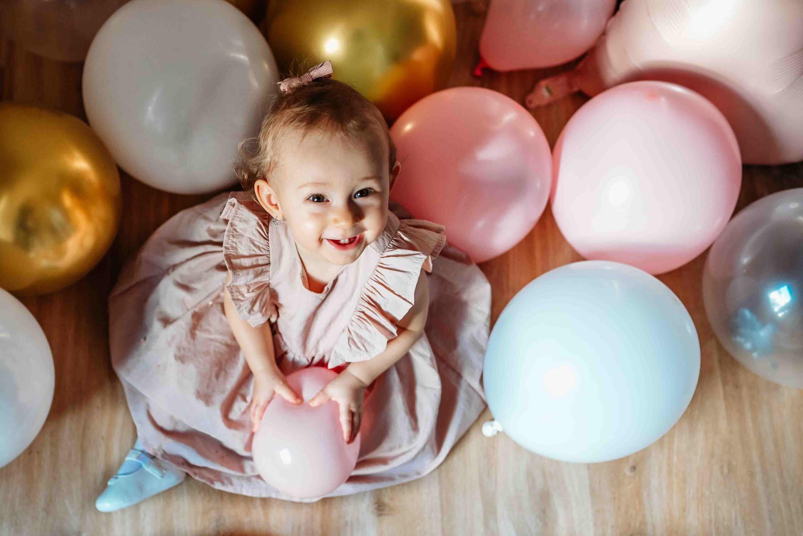 Baby girl sitting with balloons during first birthday party at home