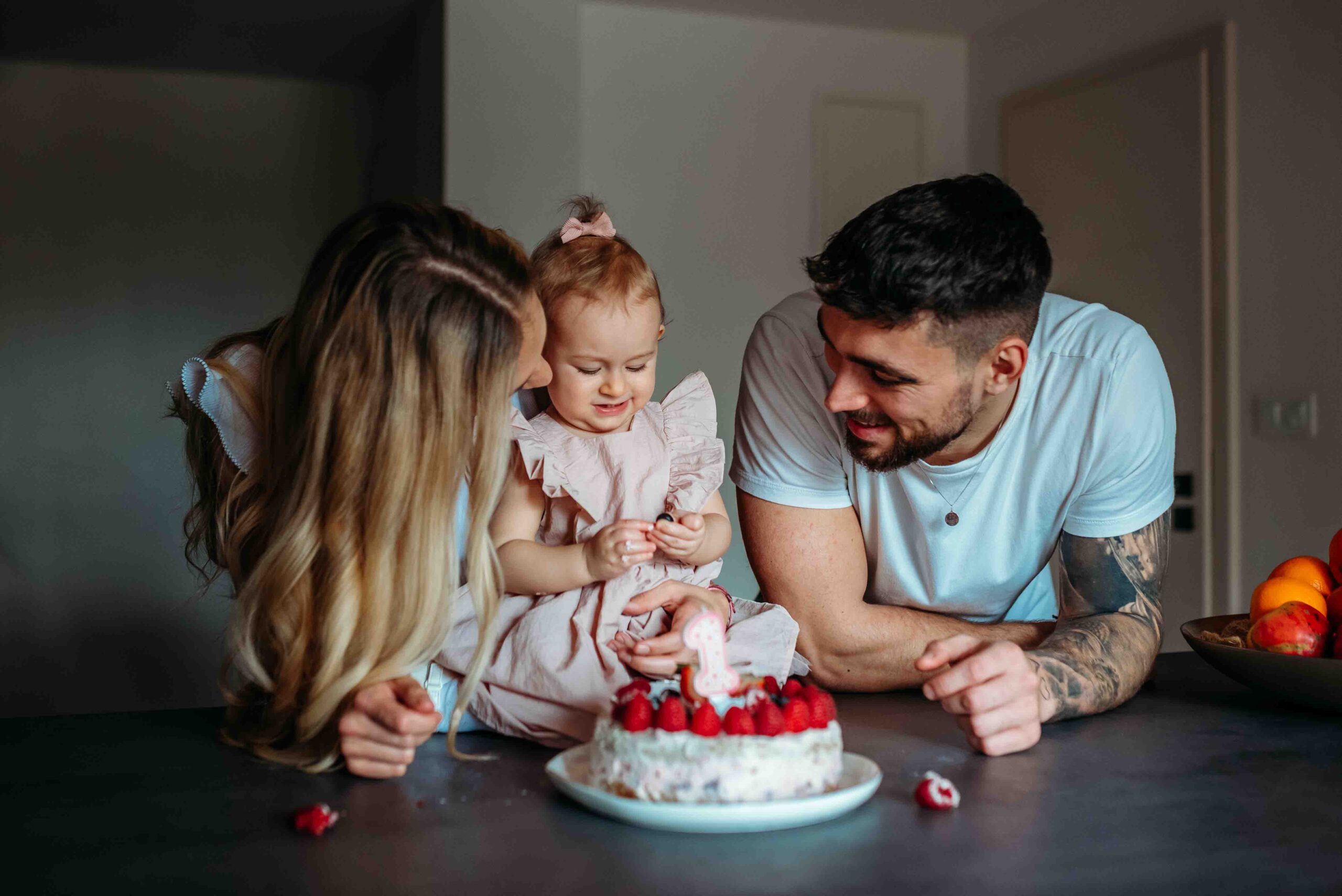 Parents and baby girl celebrating first birthday with cake at home