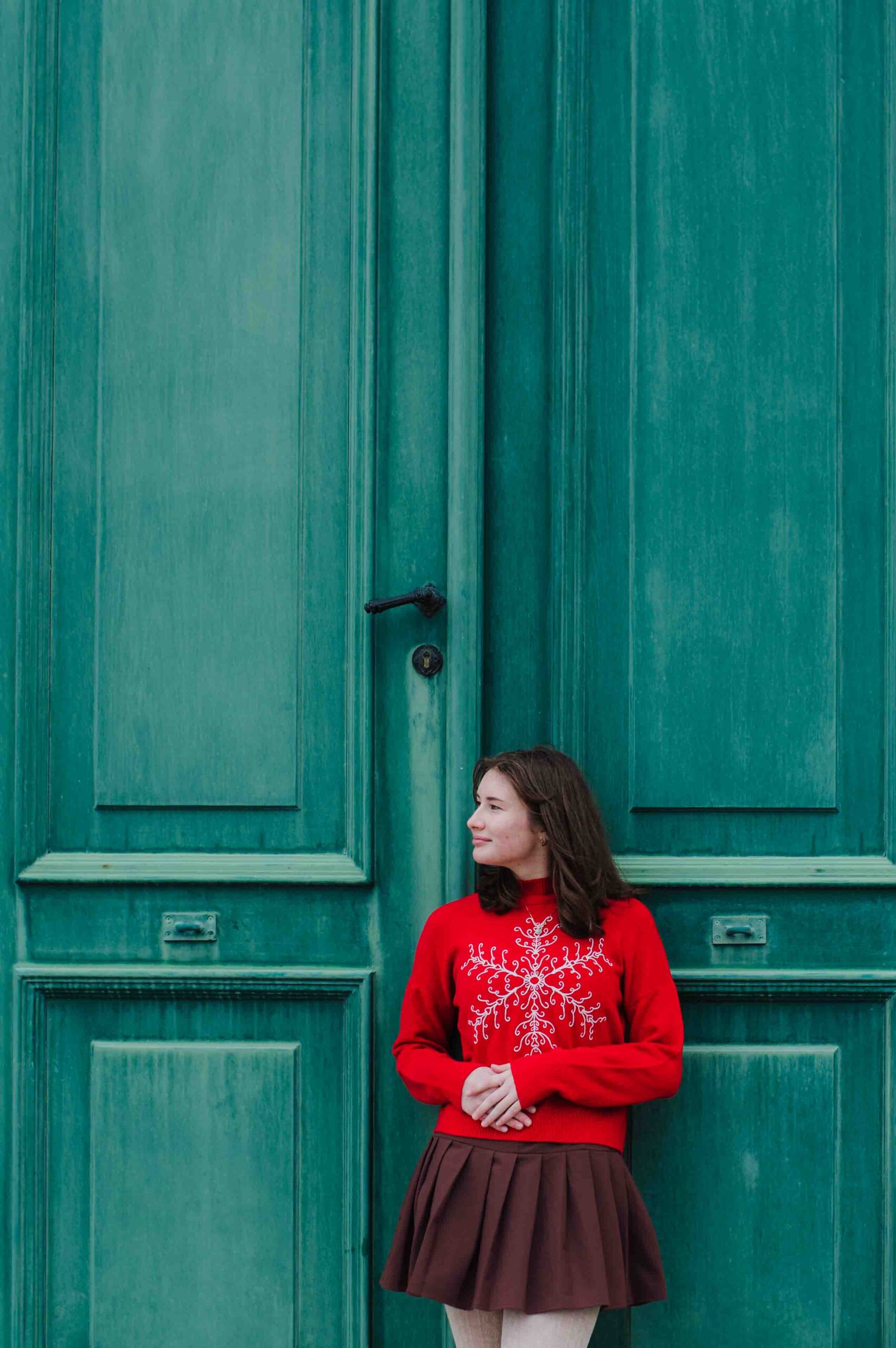 Teenage girl in red sweater posing by green doors during portrait session in Vienna