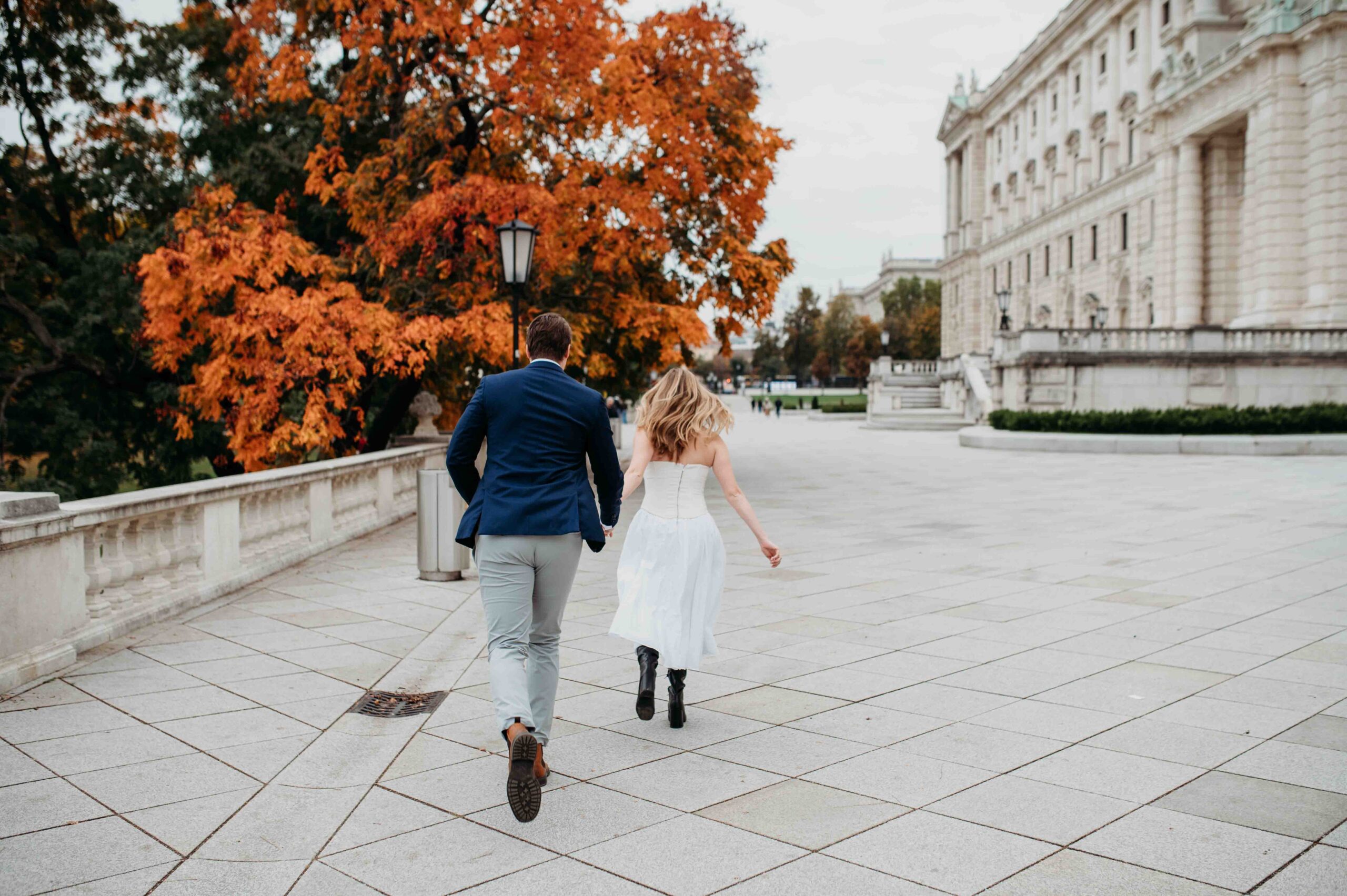 Couple running together beside autumn trees in Vienna city center