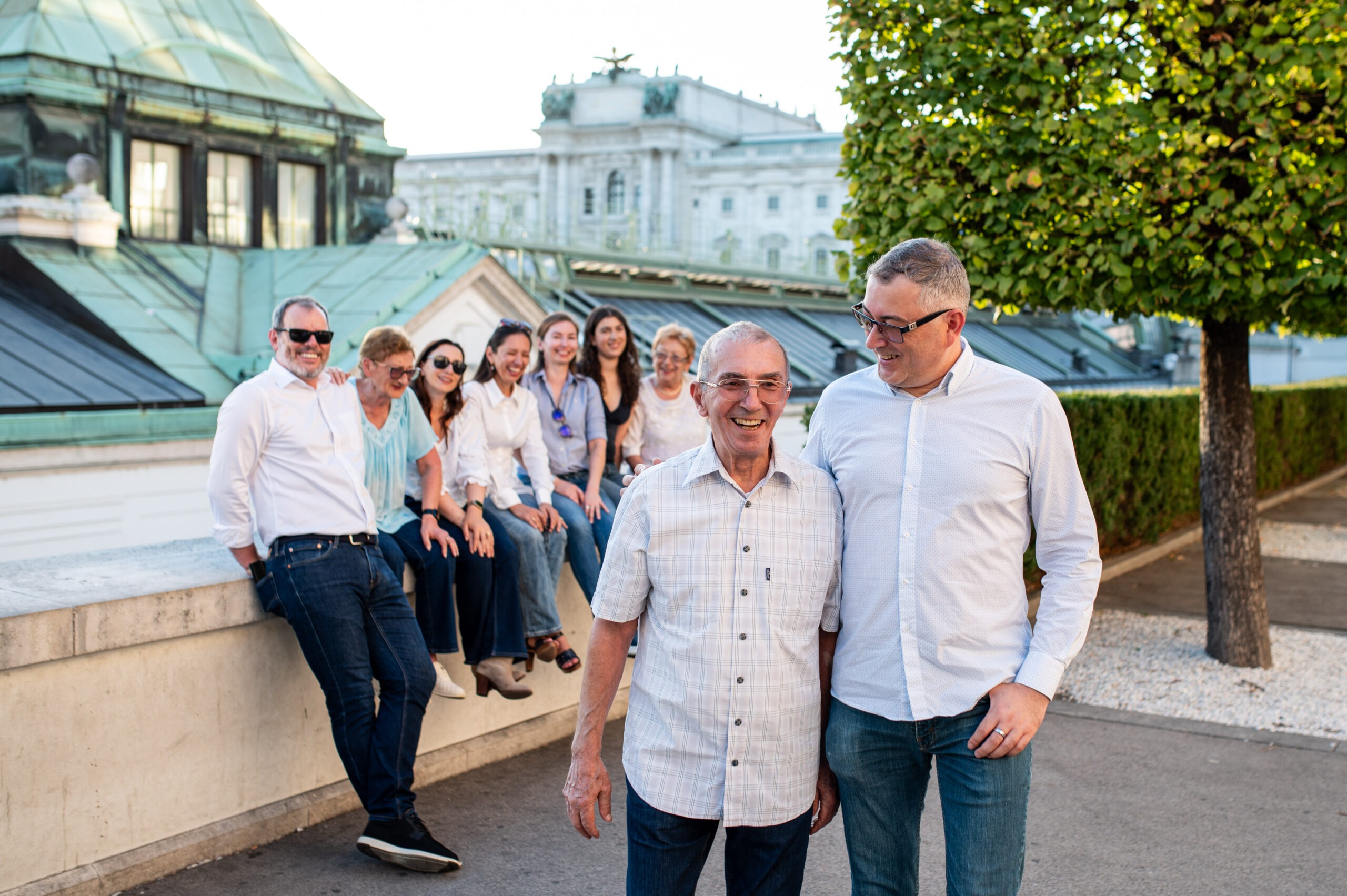 Father and adult son walking and laughing with their extended family behind them in Vienna.